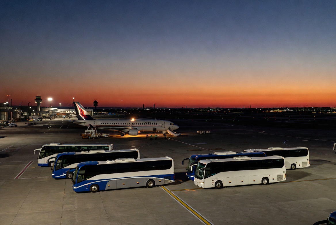 Large passenger airplane on airport tarmac at dusk with multiple emergency buses arriving for rapid passenger transfer after flight diversion
